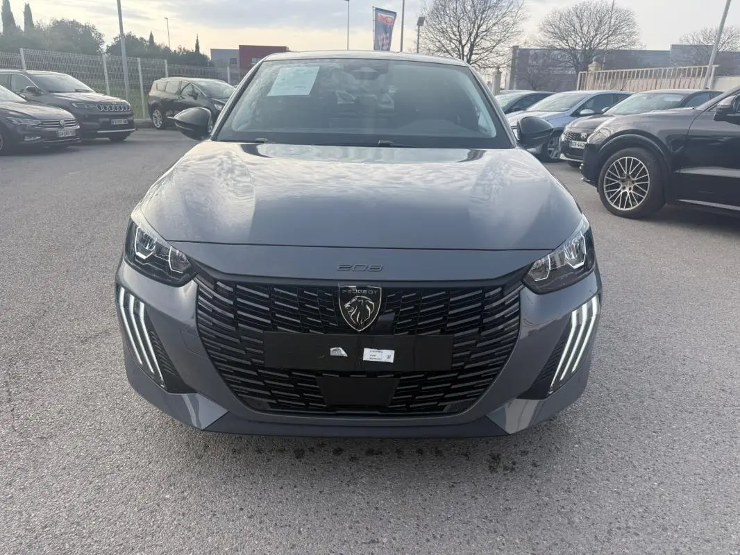 Vue frontale d'une Peugeot 208 Hybrid 110 gris métallisé, avec calandre noire et feux diurnes LED en forme de griffes.