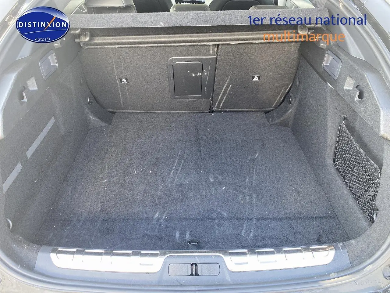 Vue plongeante sur le coffre spacieux et noir du Peugeot 408 Hybrid 145 GT e-dcs6, avec filet de rangement latéral.