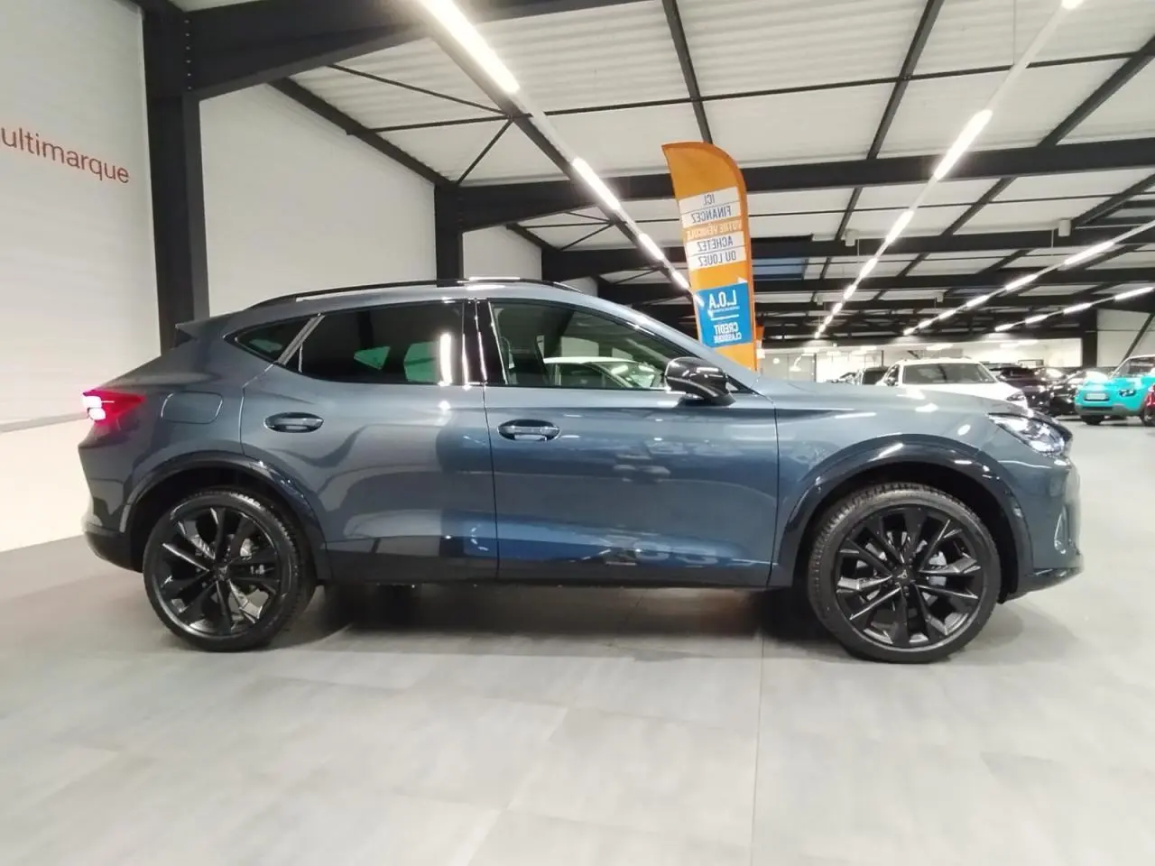 Vue latérale droite d'un CUPRA Formentor 2026 gris Magnetic Tech avec jantes alliage noires en intérieur showroom.