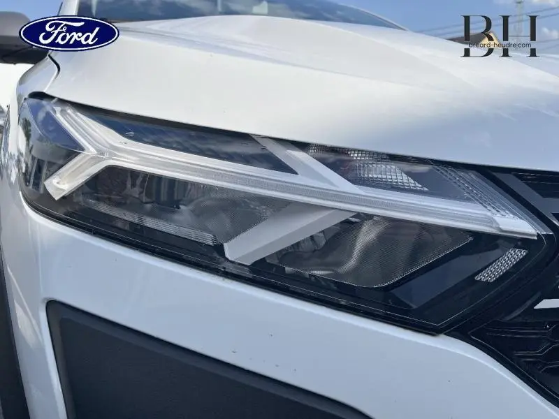 Gros plan sur le phare avant droit blanc d'une Dacia Sandero 2023 avec détails LED et calandre noire visible.