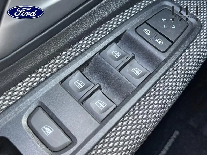 Gros plan sur les commandes des vitres électriques côté conducteur, avec habillage tissu gris et plastique noir.