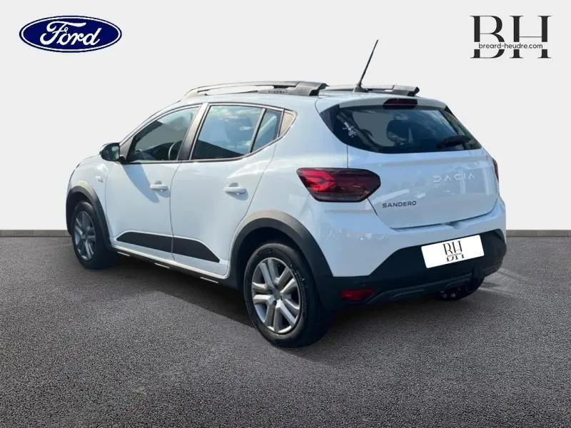 Vue 3/4 arrière droite d'une Dacia Sandero blanche avec toit ouvrant électrique et attelage visible.