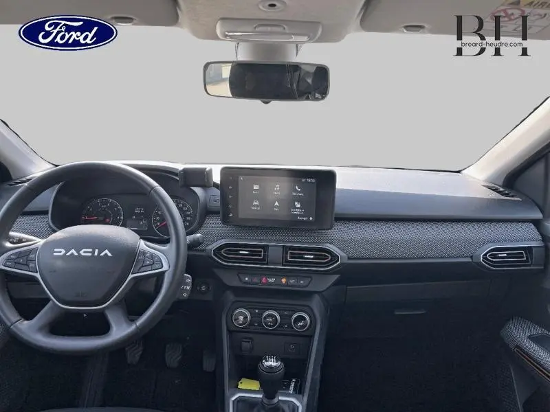 Vue intérieure avant du tableau de bord noir de la Dacia Sandero 2023 avec écran tactile et volant multifonction.