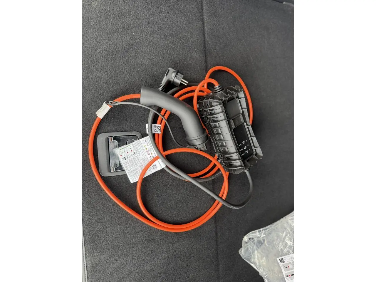 Câble de recharge orange et noir posé dans le coffre d’un Peugeot 3008 Plug-in Hybrid 2024 noir Perla.