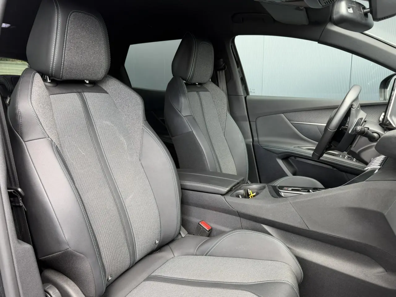 Vue intérieure côté conducteur du Peugeot 3008 2024 noir Perla, sièges bi-matière cuir et tissu gris, accoudoir central ouvert.