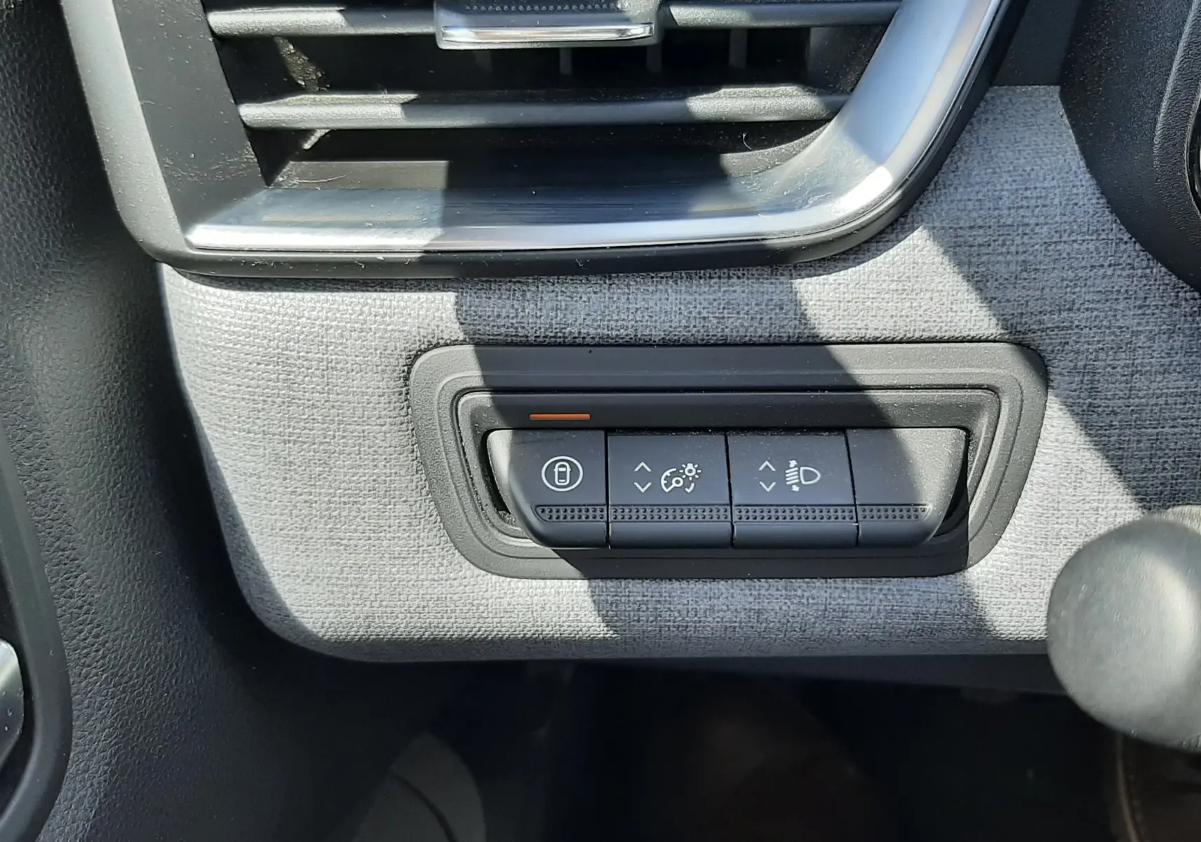 Détail intérieur montrant les commandes d’éclairage et la ventilation sur fond tissu gris d’une Renault Clio V rouge flamme.