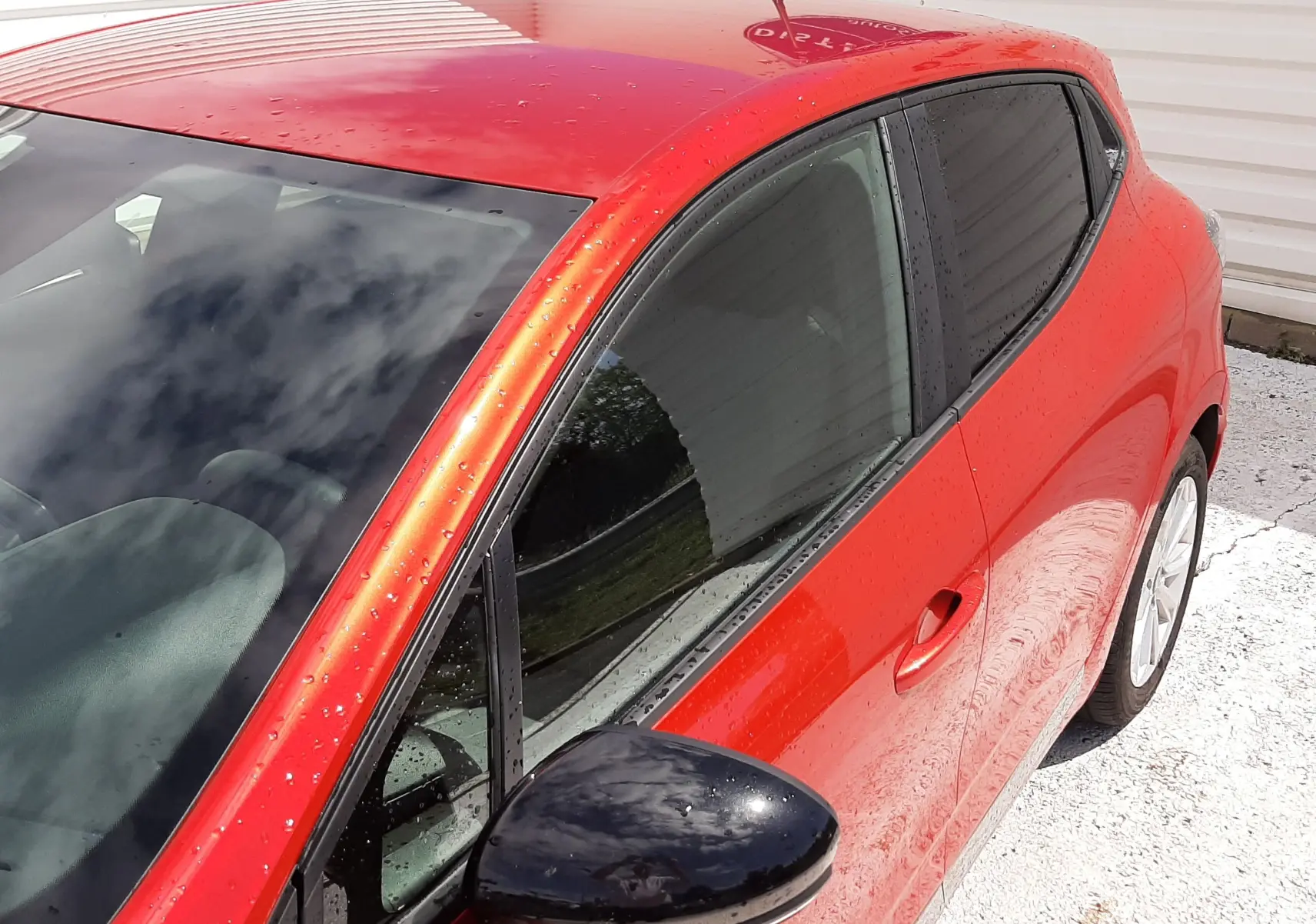 Vue 3/4 avant droit de la Renault Clio V rouge flamme avec rétroviseur noir et vitres teintées.