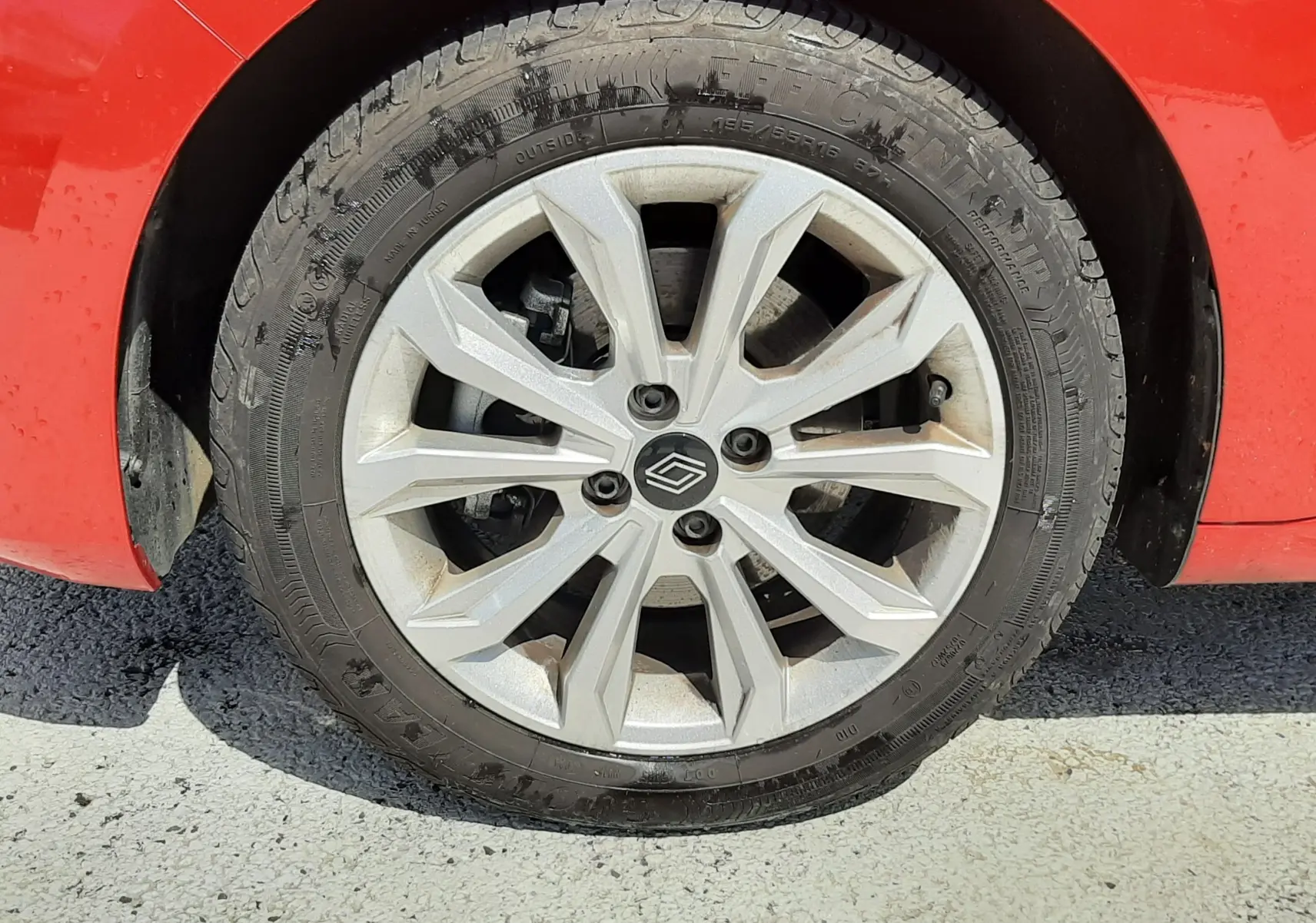 Gros plan sur la roue avant gauche d’une Renault Clio V rouge flamme, mettant en valeur la jante alliage et le pneu.