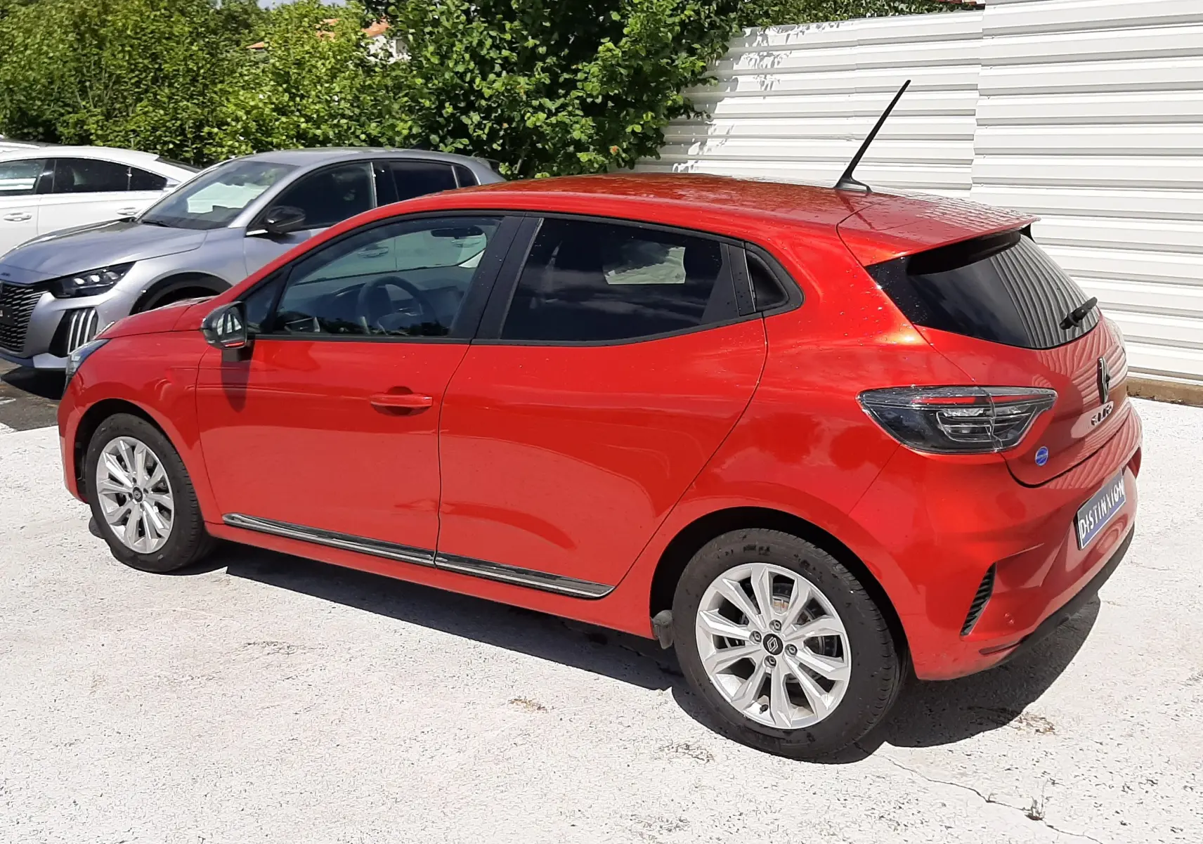 Renault Clio V rouge flamme vue de trois quarts arrière côté gauche, avec vitres teintées et jantes alliage.
