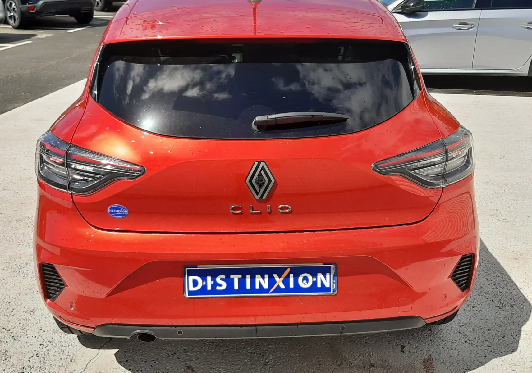 Vue arrière d'une Renault Clio V rouge flamme avec vitres arrière teintées et logo distinctif au centre du hayon.