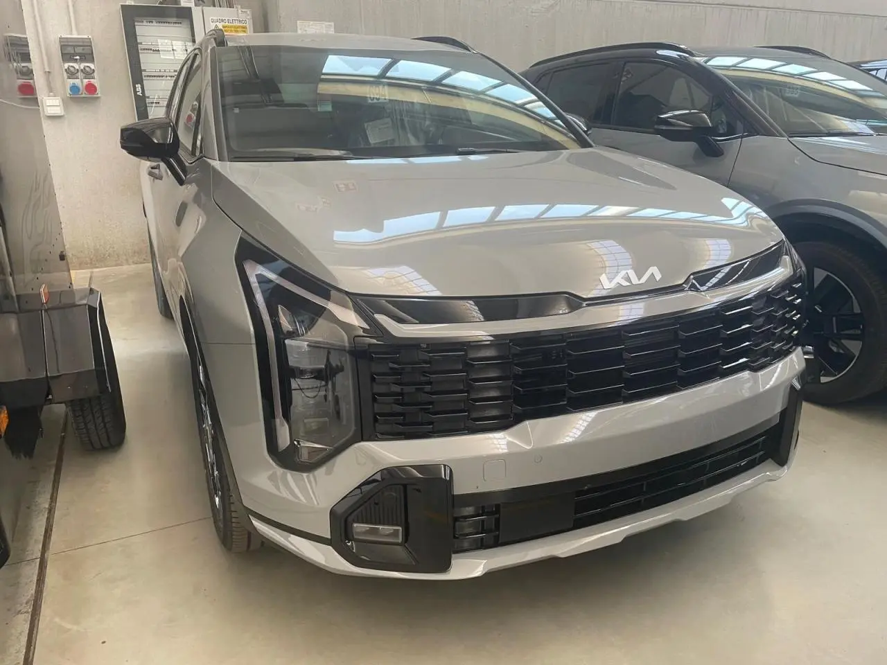 KIA SPORTAGE Hybride 239 ch GT-Line gris loup, vue 3/4 avant mettant en valeur la calandre noire et les phares LED distinctifs.