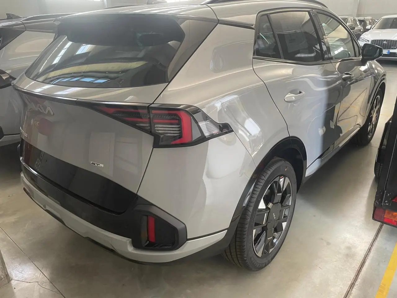 Vue 3/4 arrière droite du KIA SPORTAGE 2026 hybride gris loup avec jantes noires et feux arrière LED distinctifs.