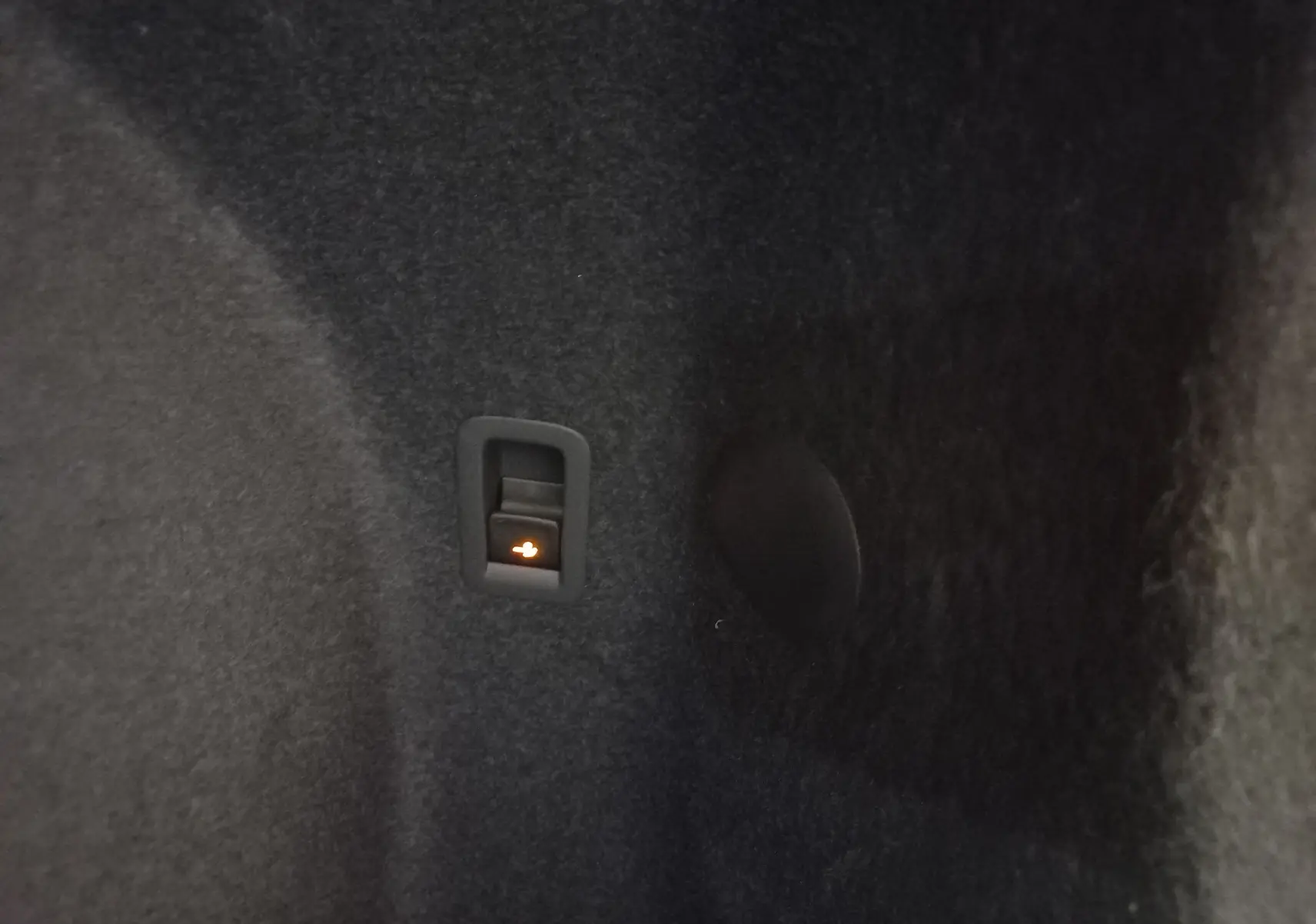 Intérieur du coffre de la CUPRA TERRAMAR 2025, détail du bouton d'ouverture électrique du hayon sur revêtement noir.