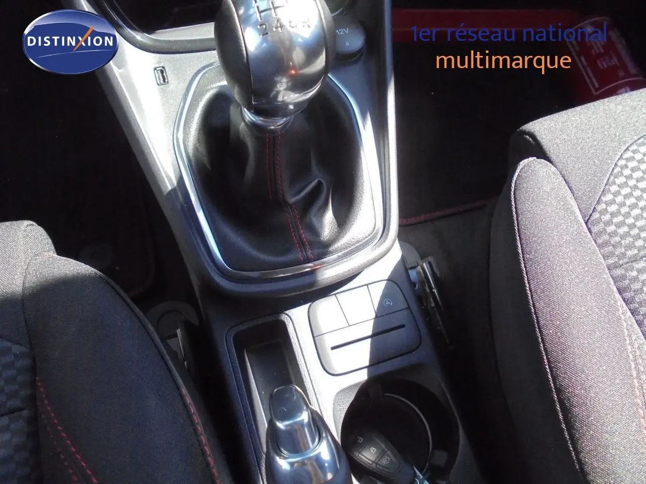 Gros plan sur la console centrale du Ford Puma 2022, montrant levier de vitesse manuel et sièges tissu noir avec surpiqûres rouges.