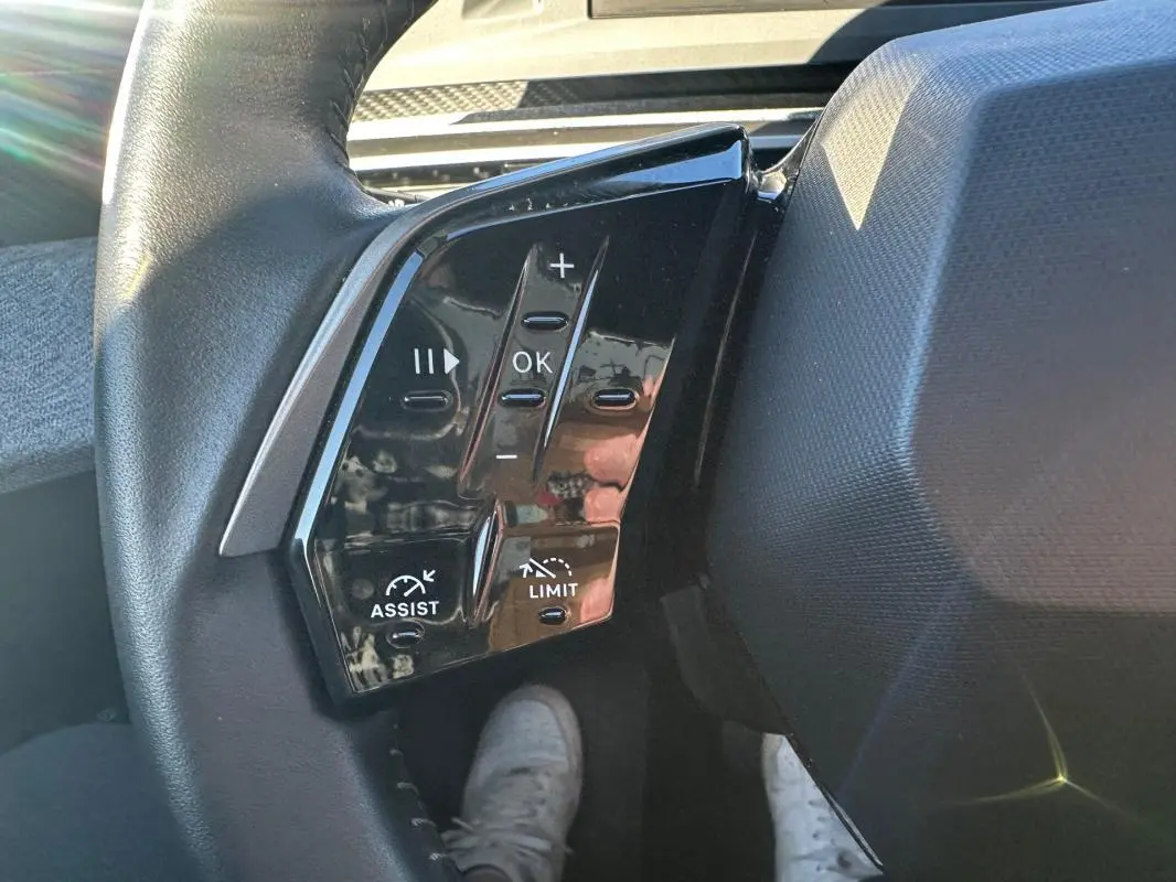 Vue rapprochée des commandes au volant gauche du Peugeot 3008 Hybrid blanc, avec boutons de régulateur et limiteur.