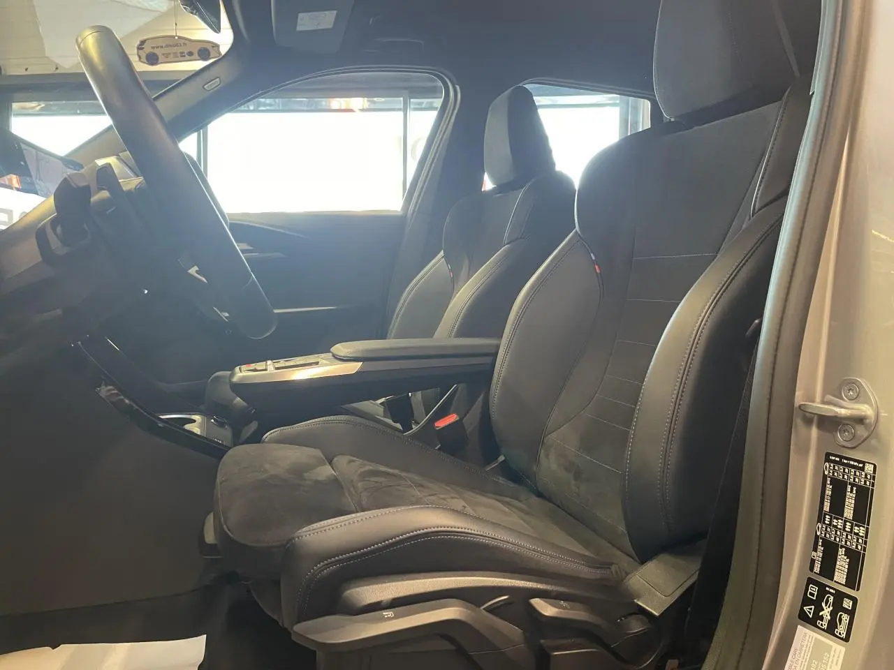 Vue intérieure côté gauche du BMW X1 xDrive 20d 2024 avec sièges M Sport en Alcantara noir et accoudoir central.