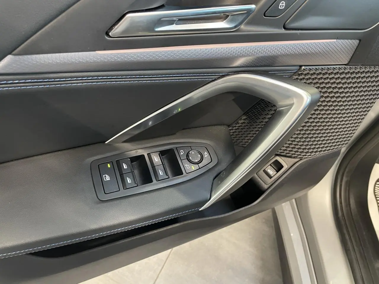 Gros plan sur la porte côté conducteur du BMW X1 xDrive 20d 2024 en Spacesilber Metallic, avec commandes des vitres et insert décoratif.