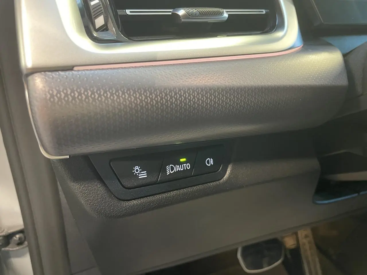 Détail des commandes d’éclairage avec bouton auto allumé sur la partie inférieure gauche du tableau de bord d’un BMW X1 Spacesilber Metallic.