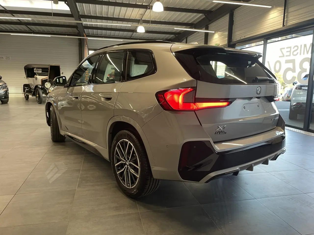 BMW X1 xDrive 20d 2024 en Spacesilber Metallic, vue 3/4 arrière droite avec feux LED allumés et jantes M Sport.