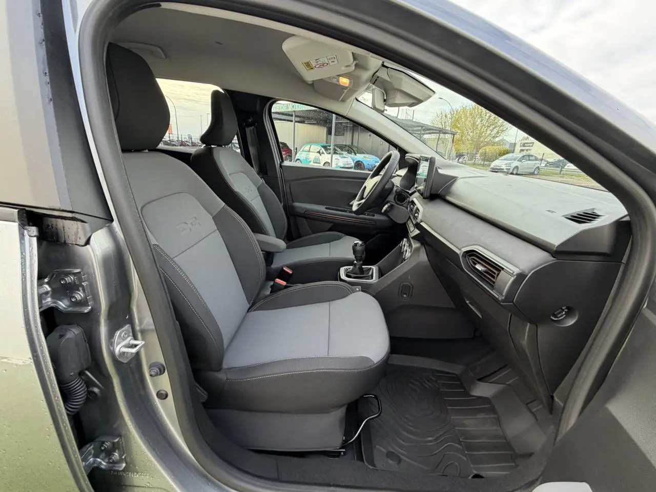 Vue intérieure côté droit du DACIA JOGGER gris shiste métal, montrant les sièges avant gris et la console centrale avec levier de vitesse manuel.