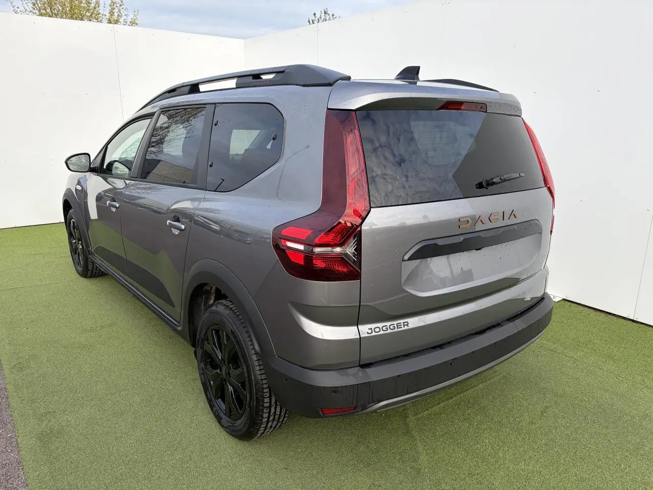Vue 3/4 arrière droite d'un Dacia Jogger gris schiste métal avec barres de toit noires et jantes noires.