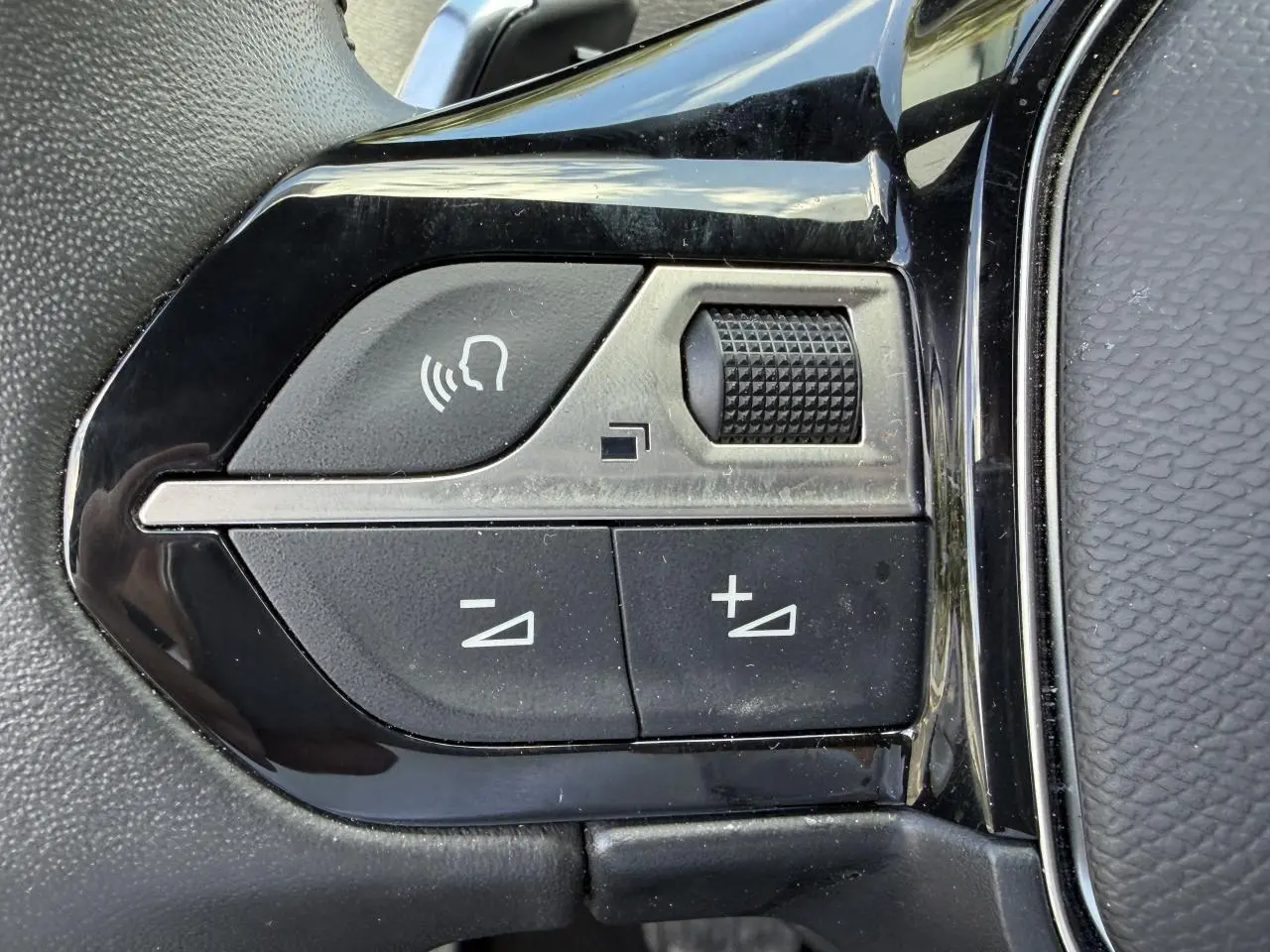 Gros plan sur les commandes de volume et de reconnaissance vocale sur le volant noir du Peugeot 3008 Plug-in Hybrid 2024.