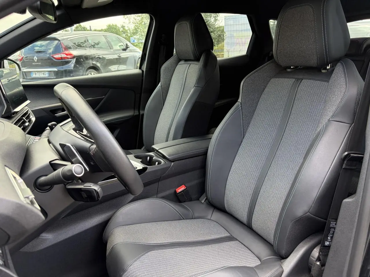 Vue intérieure côté conducteur du Peugeot 3008 2024, sièges bi-matière gris et noir avec accoudoir central.