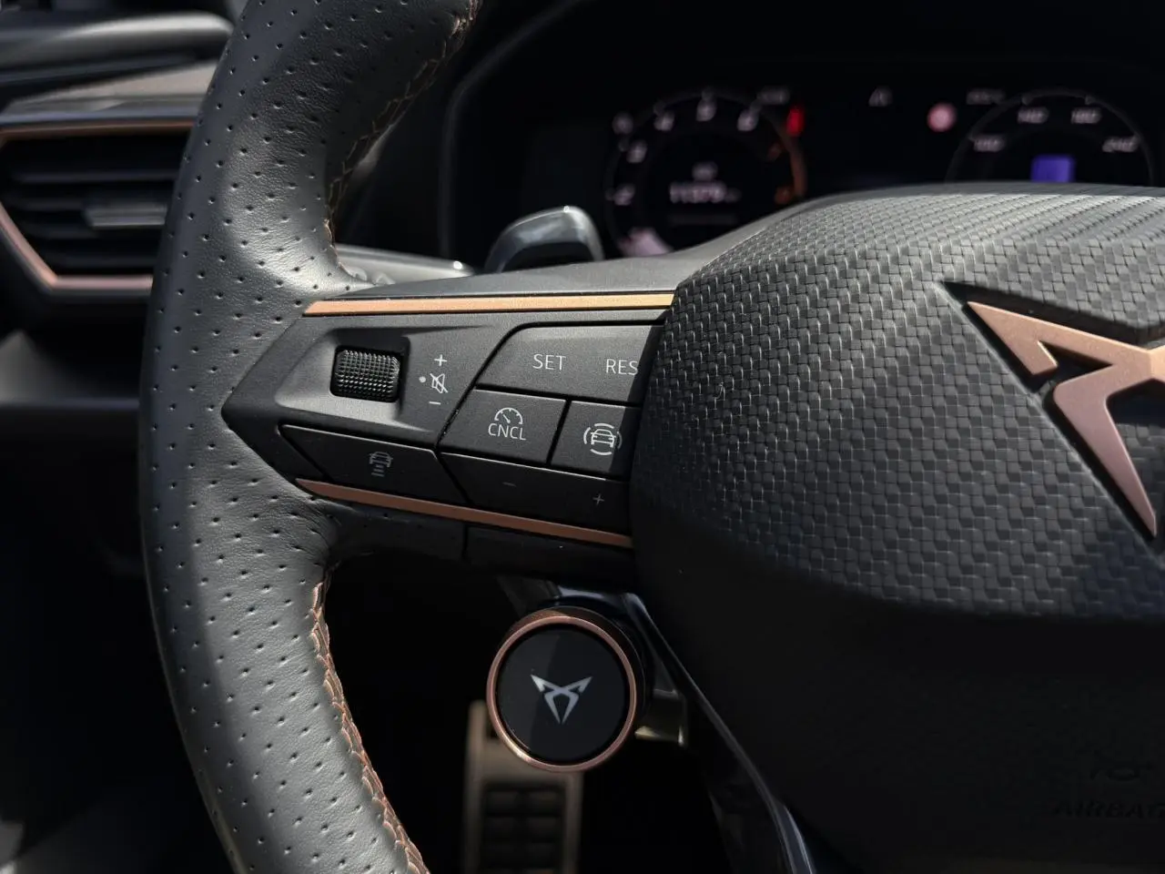 Gros plan sur le volant perforé noir avec logo CUPRA cuivré et commandes multifonctions à gauche, intérieur du Formentor 2025.