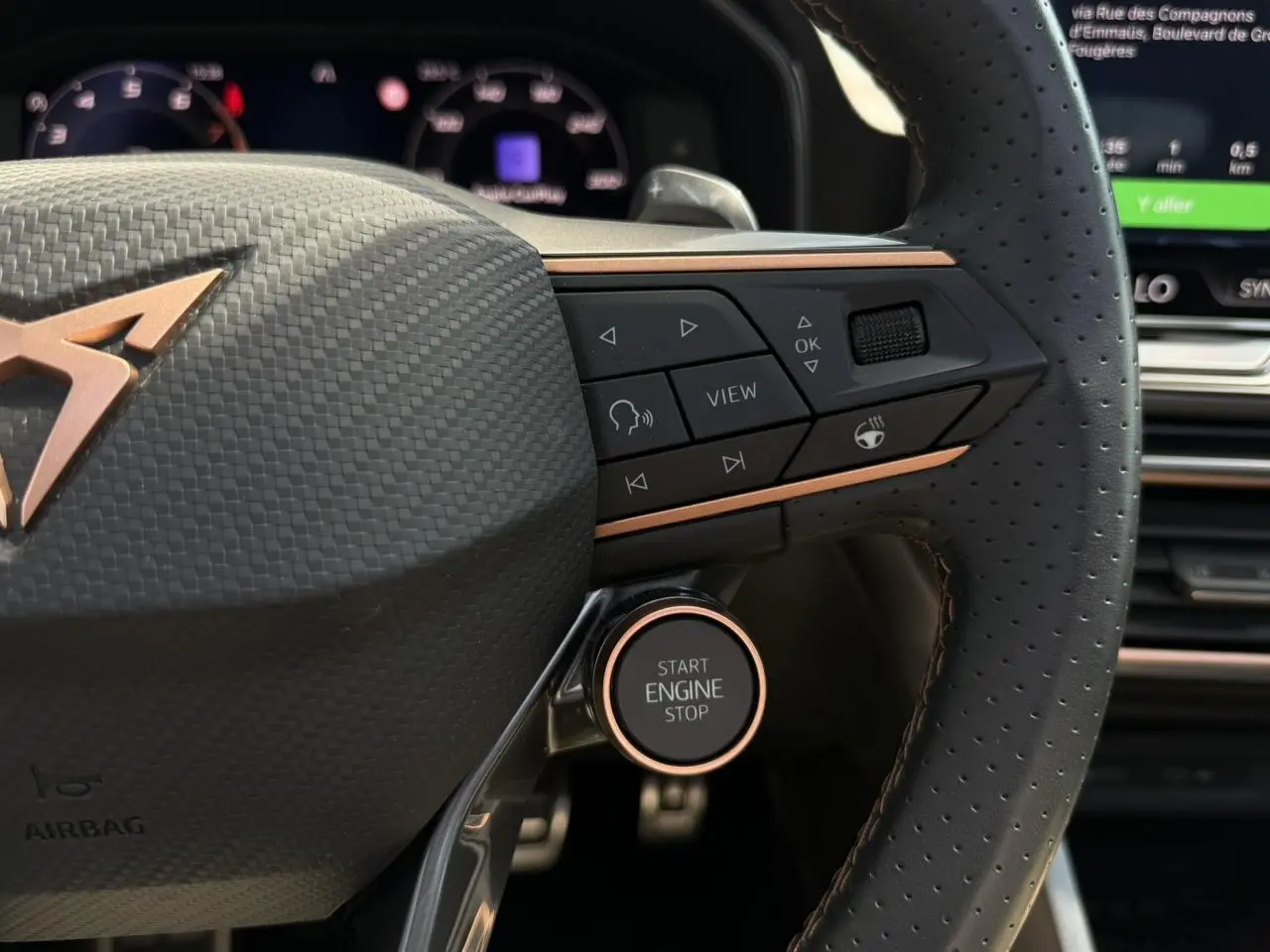 Gros plan sur le volant perforé noir avec logo CUPRA cuivre et bouton Start Engine Stop dans un intérieur moderne.