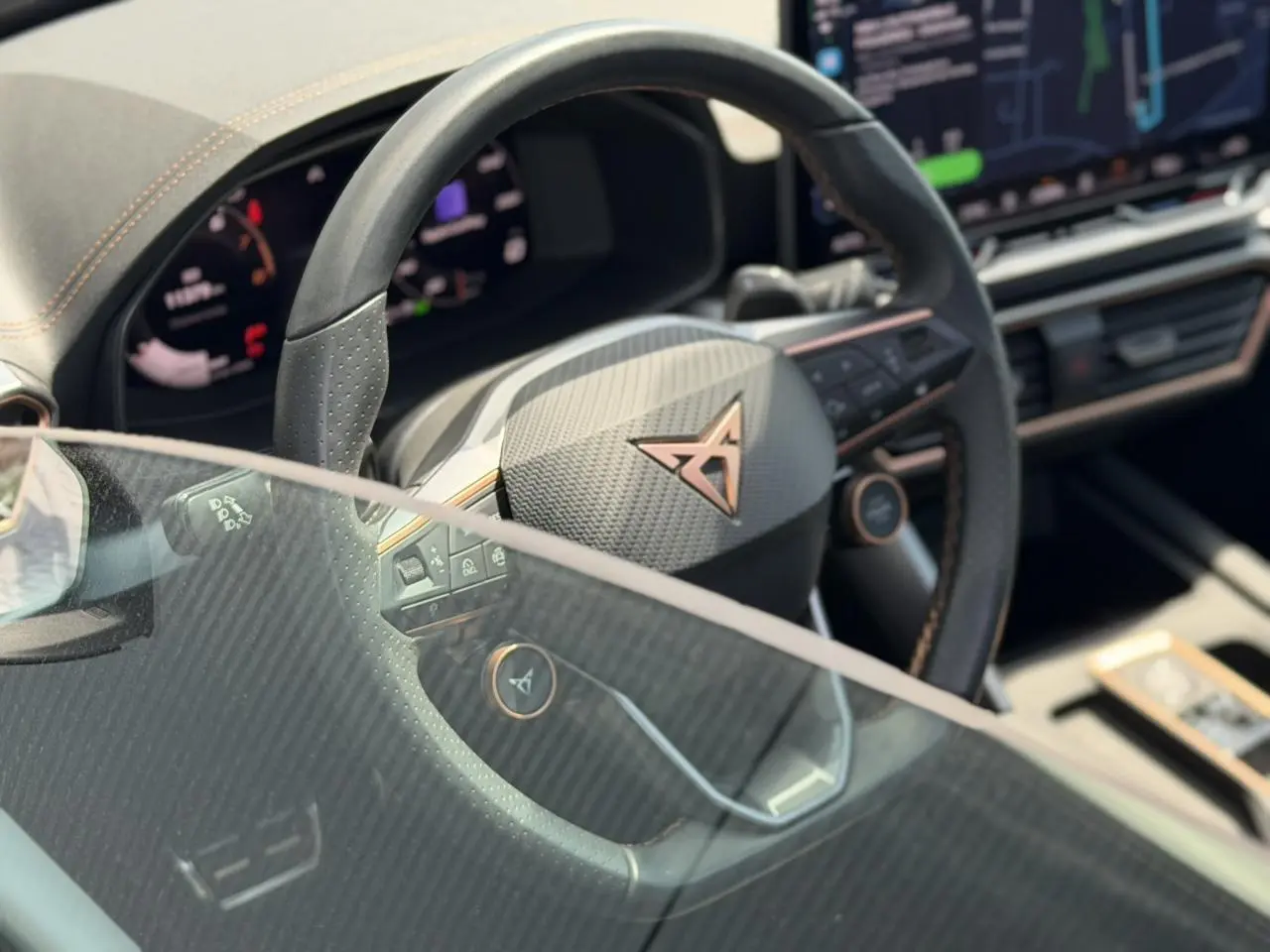 Gros plan sur le volant noir perforé avec logo CUPRA cuivré et tableau de bord numérique partiellement visible.