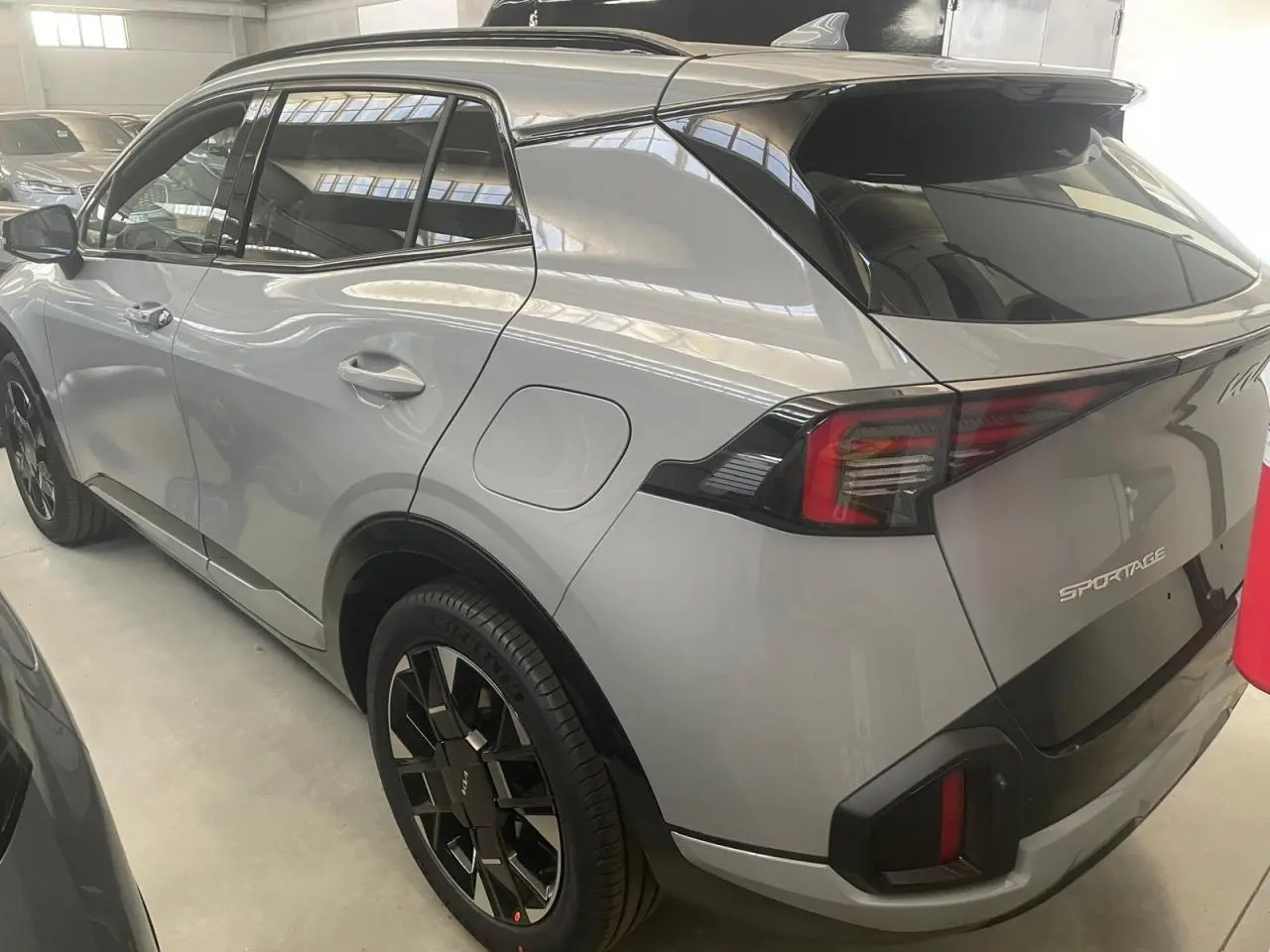 Vue 3/4 arrière droite du KIA SPORTAGE hybride gris lunaire 2026 avec jantes noires et feux arrière LED distinctifs.