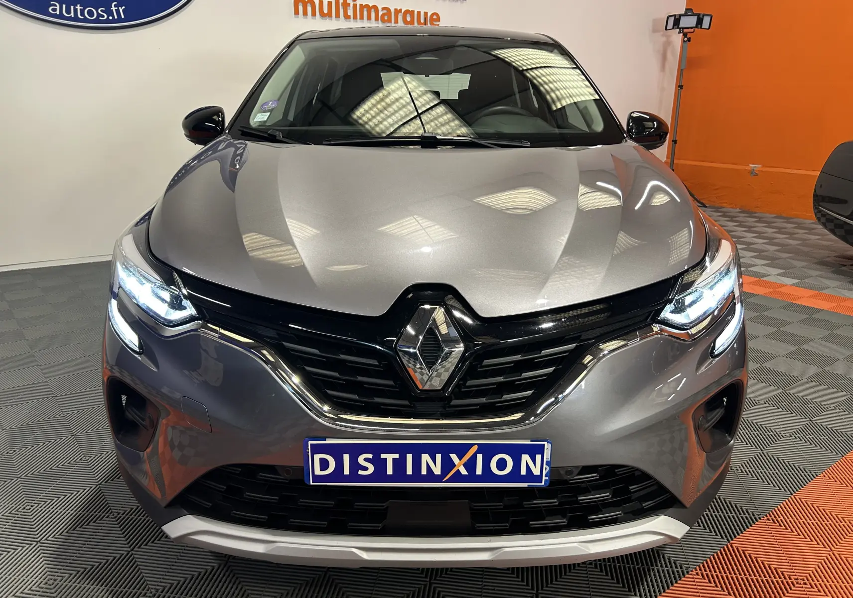 Vue avant rapprochée d’un Renault Captur gris 2022 avec phares allumés et calandre noire brillante.