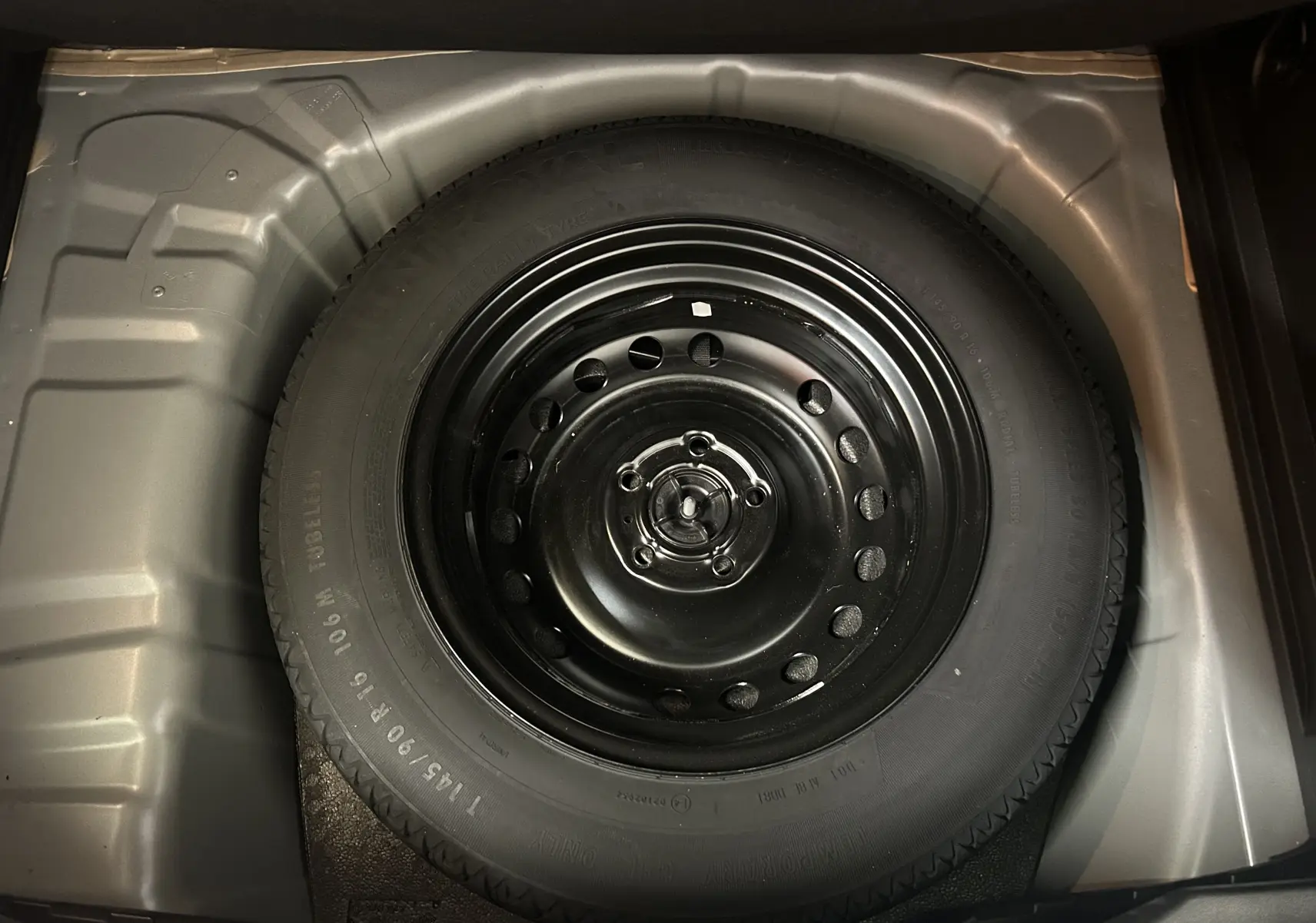 Vue en plongée sur la roue de secours noire logée dans le coffre gris d’un Renault Captur 2022.