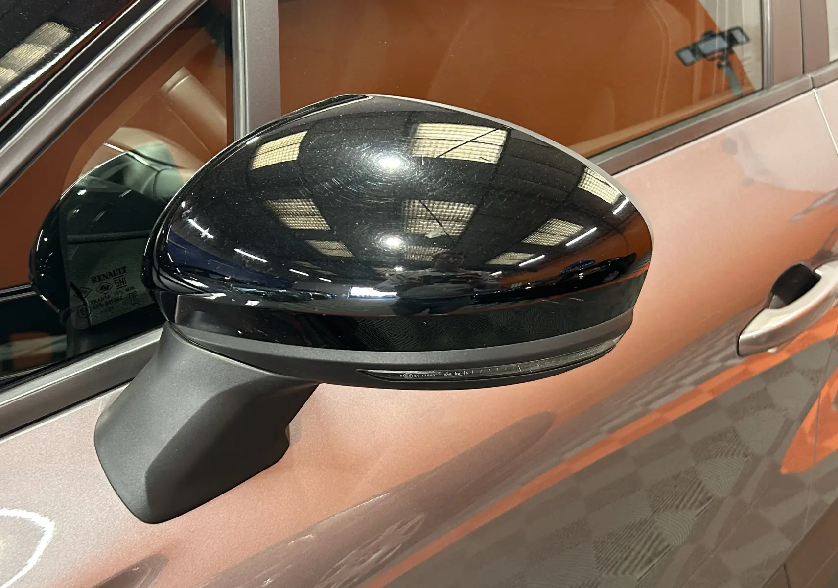 Gros plan sur le rétroviseur noir côté gauche du Renault Captur gris, avec reflet lumineux sur la carrosserie.