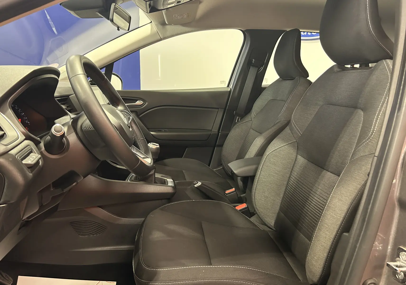 Vue intérieure côté gauche du Renault Captur gris 2022, montrant les sièges avant en tissu et le volant avec boîte manuelle.