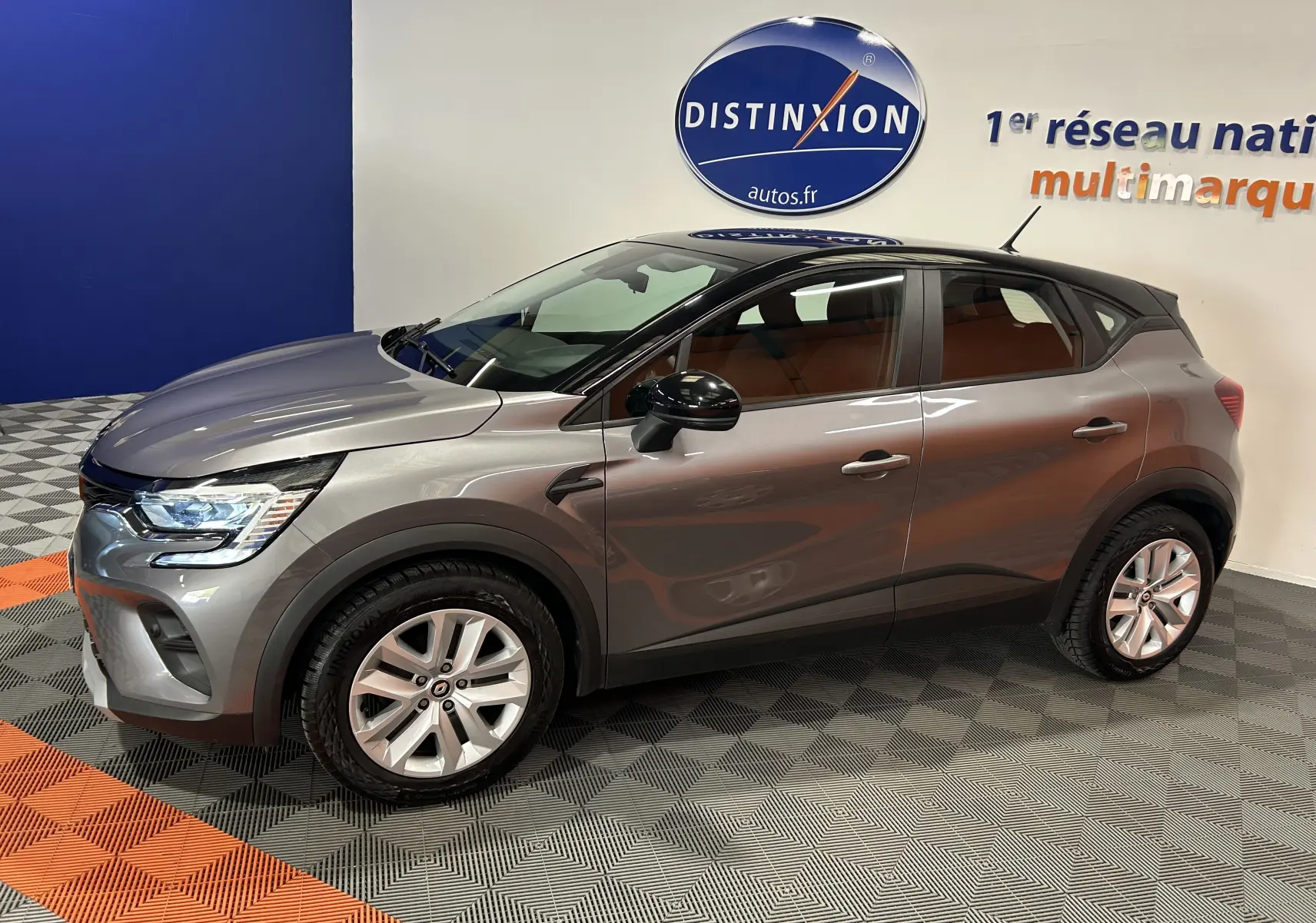 Renault Captur gris en vue de profil côté gauche, avec jantes alliage et rétroviseurs noirs, en intérieur showroom.