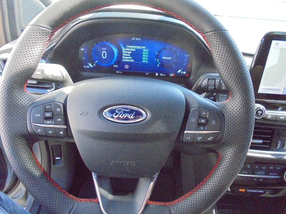 Vue rapprochée du volant perforé avec surpiqûres rouges et tableau de bord digital bleu d'une Ford Puma gris Solar Metal 2022.