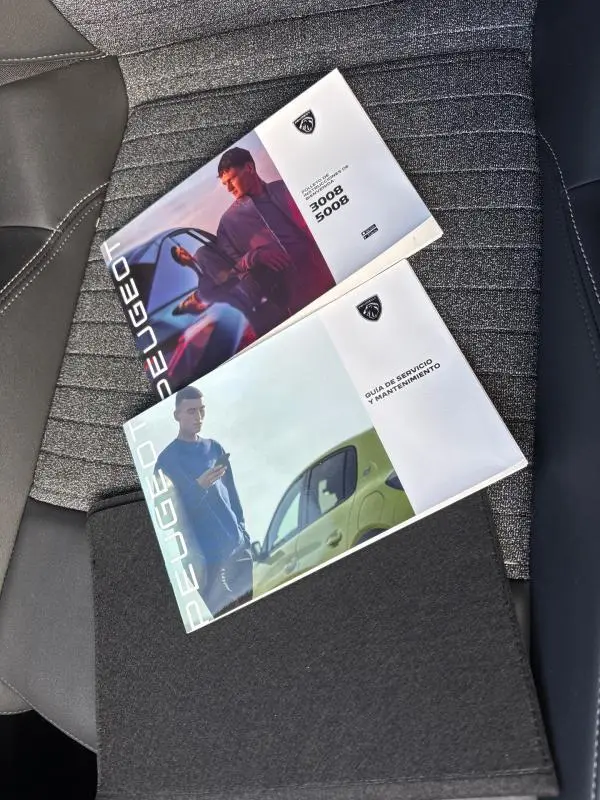 Image montrant deux brochures Peugeot posées sur un siège de voiture gris, avec détails de textures et coutures visibles.