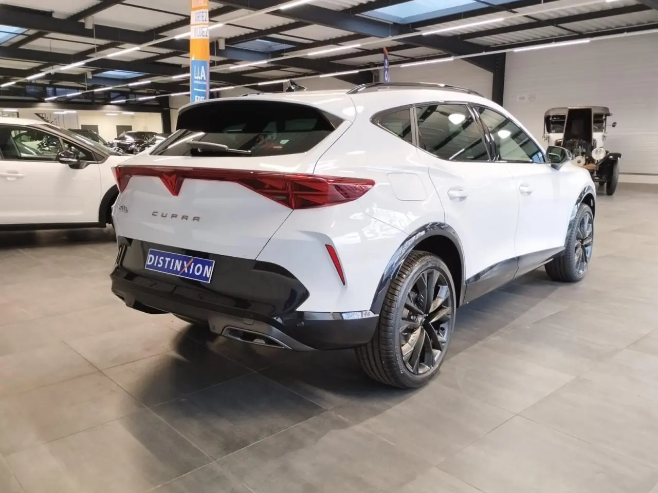Vue 3/4 arrière droite du CUPRA Formentor blanc Nevada avec jantes noires et éléments noirs contrastants en intérieur showroom.