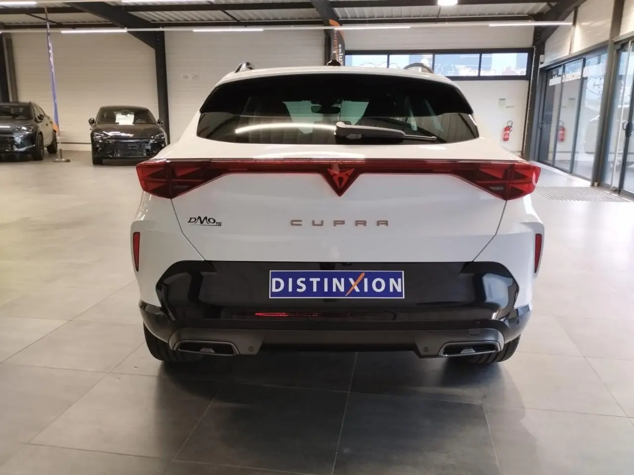 Vue arrière d'un CUPRA Formentor blanc Nevada avec feux arrière en bandeau lumineux et double sortie d'échappement noire.