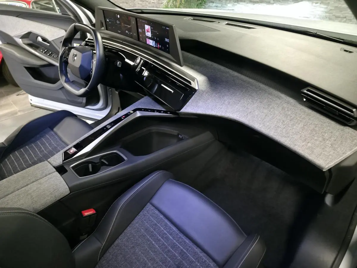 Intérieur avant droit du Peugeot 3008 2025 avec tableau de bord gris chiné et sièges tissu bleu et cuir noir.