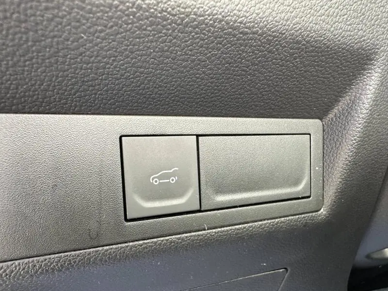 Bouton d'ouverture du coffre sur panneau intérieur noir de la Renault Symbioz rouge, vue rapprochée.