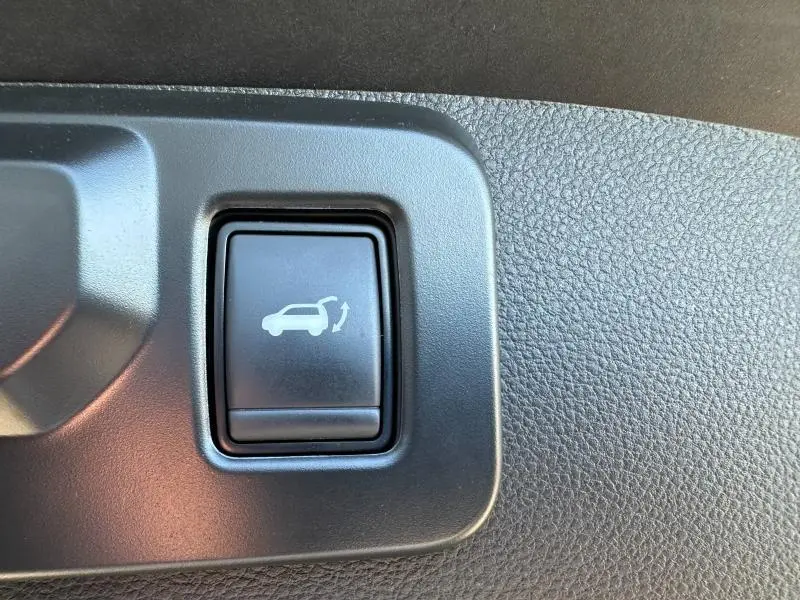 Gros plan sur le bouton d'ouverture électrique du coffre dans l'habitacle noir du Renault Symbioz rouge.