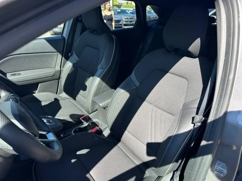 Vue intérieure côté gauche des sièges avant noirs du Renault SYMBIOZ 1.6 E-Tech 2025 avec accoudoir central et volant multifonction.