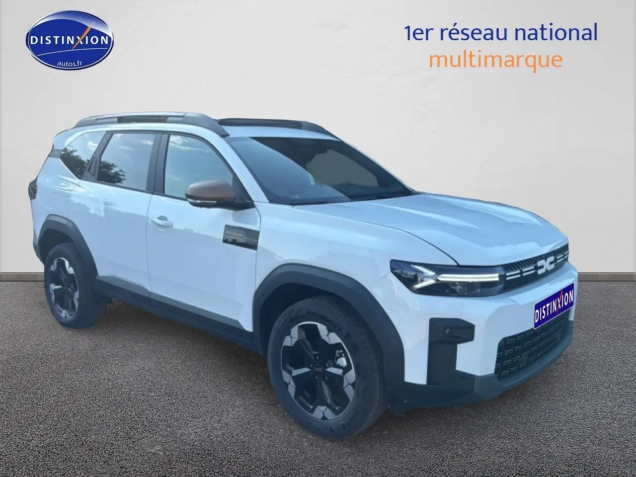 SUV Dacia Bigster blanc en 3/4 avant droit avec jantes noires et barres de toit visibles.