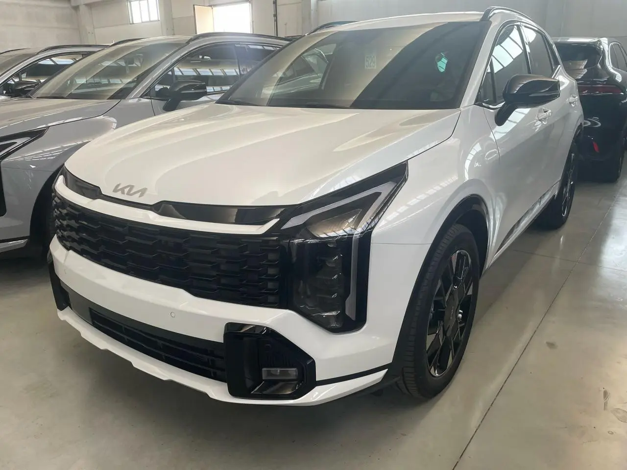 Vue 3/4 avant d'un KIA SPORTAGE hybride blanc 2026 avec calandre noire et jantes noires distinctives.