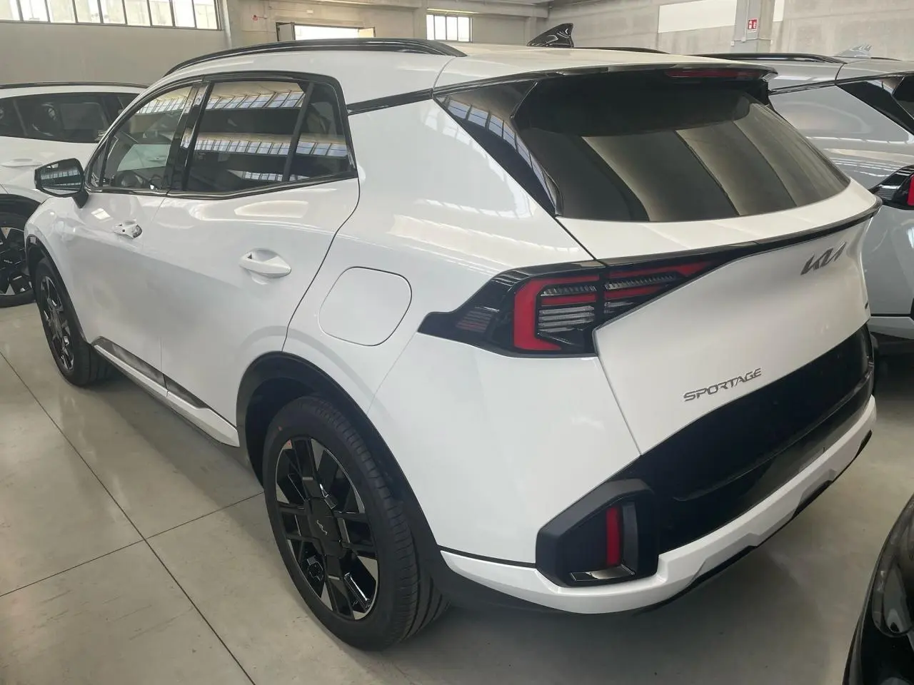 Vue 3/4 arrière droite du KIA Sportage blanc hybride 2026 avec jantes noires et feux arrière LED distinctifs.