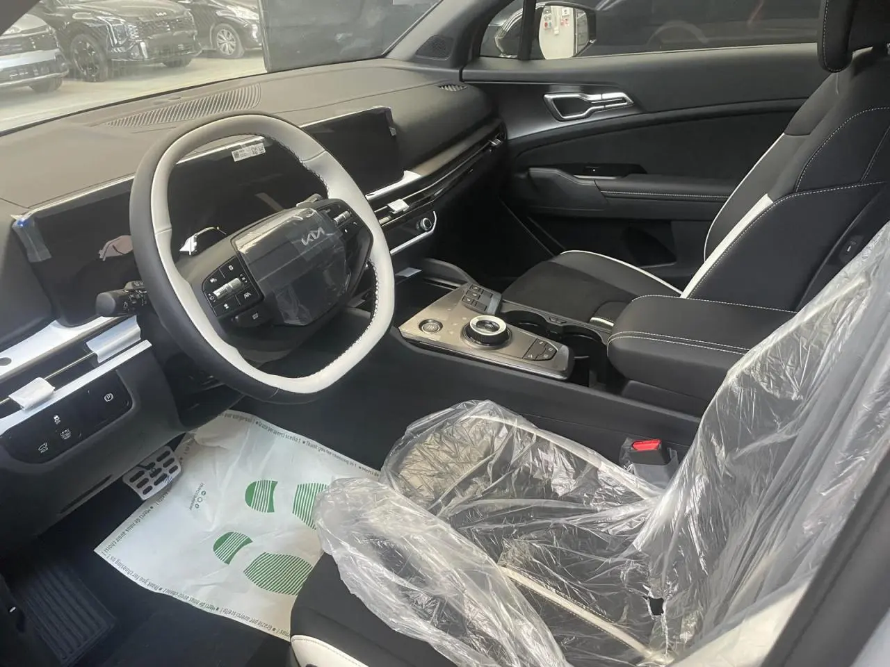 Intérieur avant droit du Kia Sportage 2026 hybride blanc, avec volant multifonction et sièges protégés par film plastique.