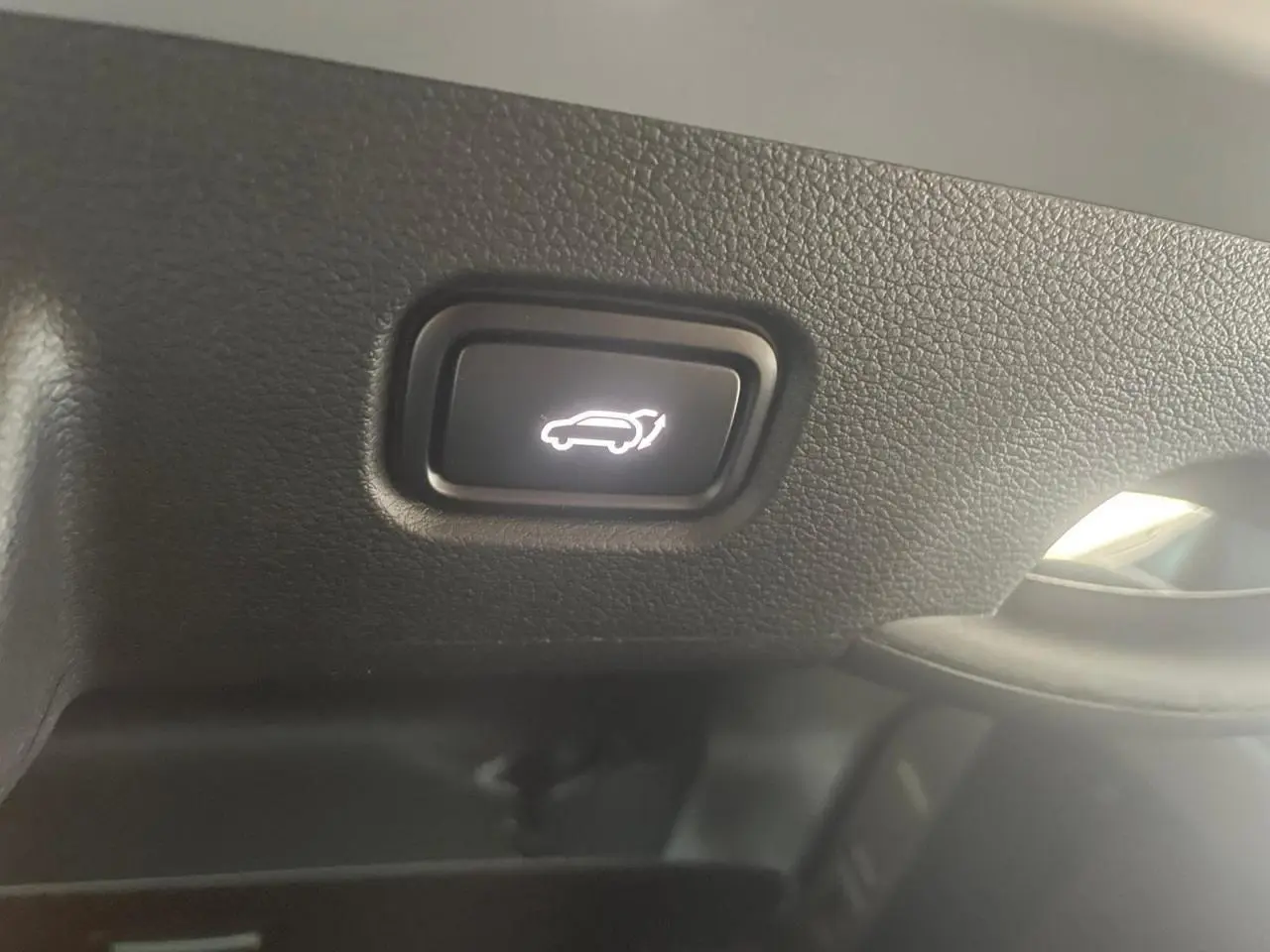 Bouton intérieur noir avec symbole blanc d'ouverture du coffre sur KIA SPORTAGE Hybride 2026, vue rapprochée du tableau de bord.