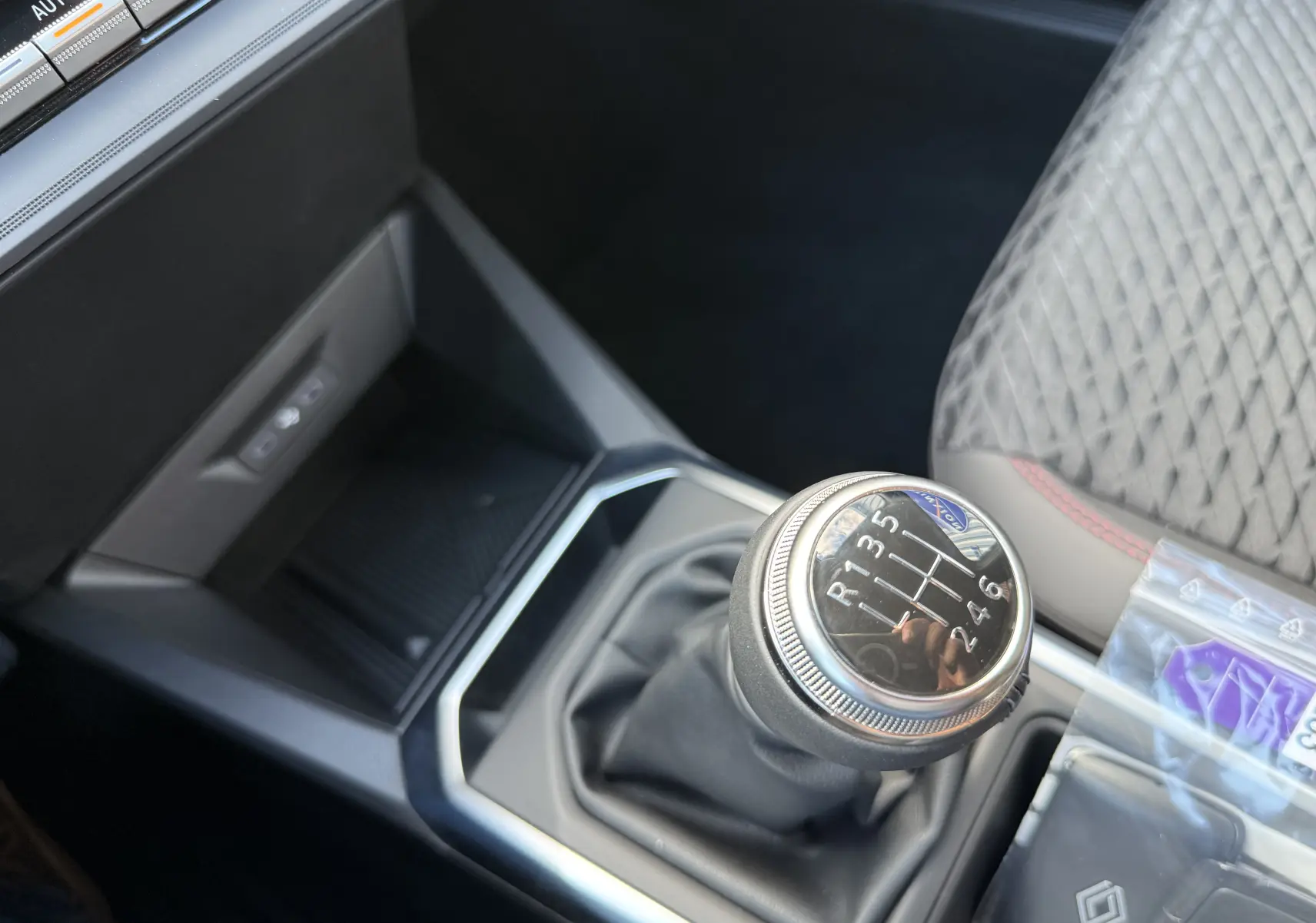 Gros plan sur le levier de vitesses manuel de la Renault Clio VI TCe 115 Techno, intérieur gris avec surpiqûres rouges.